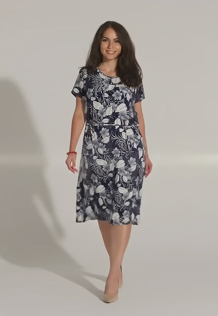 Видео представяне в студийна среда с неутрален фон, където макси модел върви бавно към камерата, облечена в Елегантна лятна рокля с джобове и флорален десен