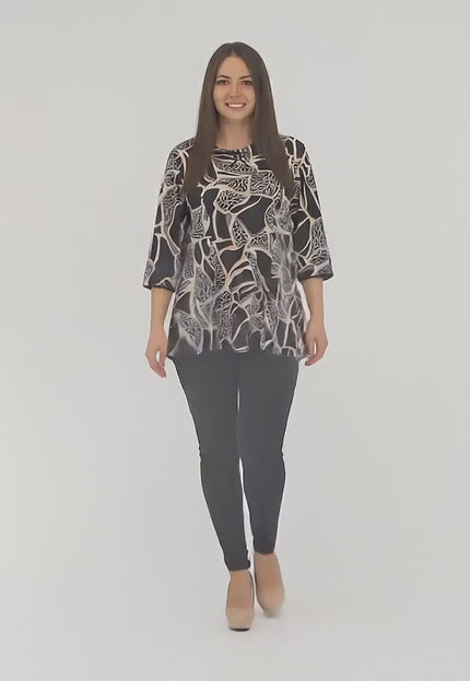 Студийно видео на макси модел на неутрален фон, който върви бавно към камерата и носи Разкроена туника с абстрактен принт и декоративна панделка