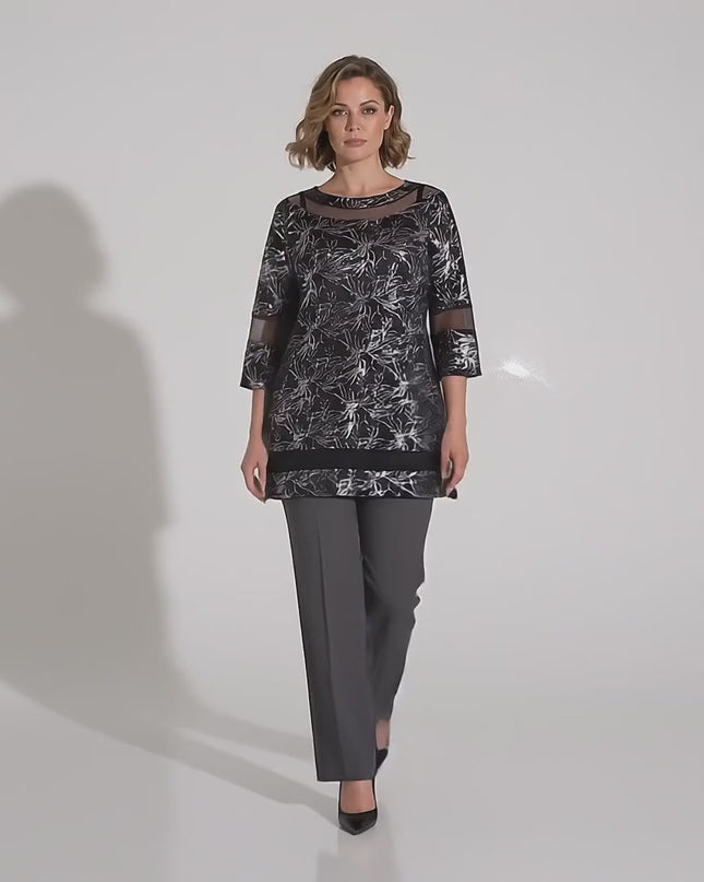 Продуктово видео в студио с неутрален фон, показващо макси модел, която върви бавно към камерата, облечена с Черна официална макси туника с мрежести детайли и сребрист принт