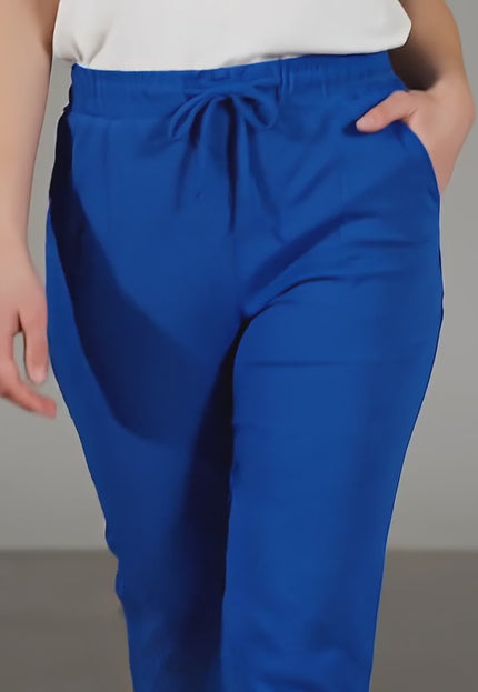 Видео в студийна среда показващо как модел носи Дамски панталон големи размери в кралскосин цвят с ластик и връзки и върви бавно към камерата на неутрален фон