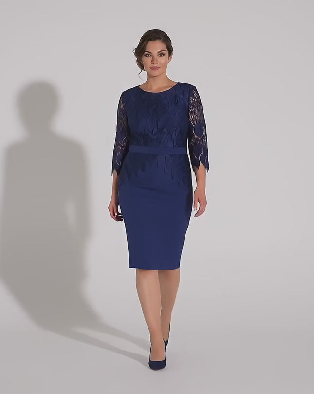 Плюс сайз модел върви бавно към камерата в студио с неутрален фон, облечена в Елегантна тъмносиня макси рокля с дантела и колан