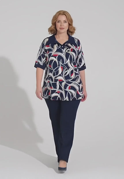 Студийно видео, в което модел носи Елегантна разкроена туника големи размери в шарен десен и върви бавно към камерата на неутрален фон