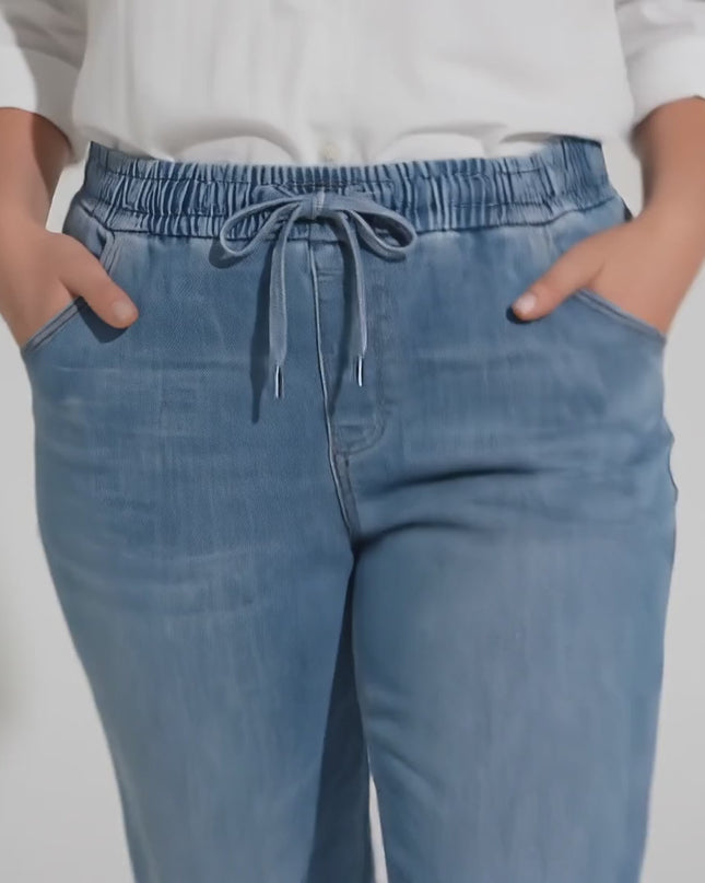 Студийно видео, в което плюс размер модел върви бавно към камерата на неутрален фон, облечена в продукта Сини макси дамски дънки с ластик и връзки от тенсел и памук