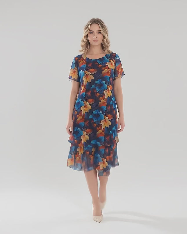 Продуктово видео в студио с неутрален фон, показващо плюс сайз модел, който върви бавно към камерата, носейки Официална тъмносиня макси рокля от шифон с многоцветен принт на листа