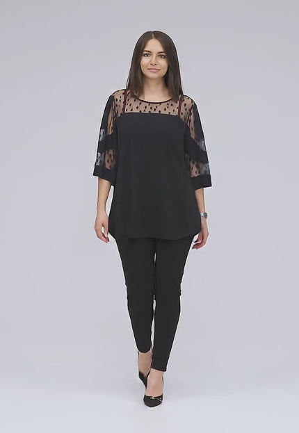 Макси модел, облечена в Черна официална туника с тюл на точки и 3/4 ръкави, върви бавно към камерата в студийна среда на неутрален фон