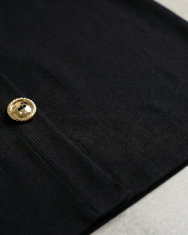 Детайл отблизо на официална черна рокля, показващ ефектно декоративно златисто копче и структурата на еластичното рипсено плетиво.