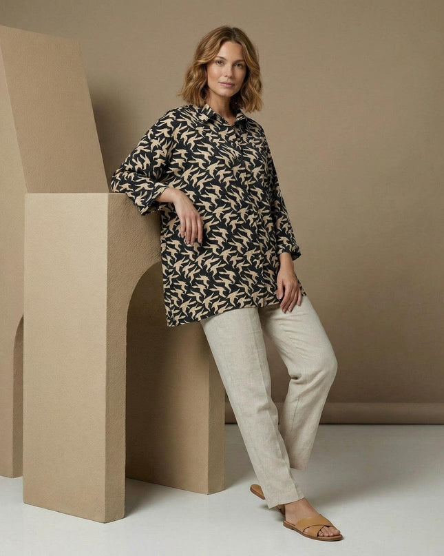 Цял ръст на модел, облечен в разкроена макси риза с птичи десен в черно и бежово, съчетана със светъл панталон.