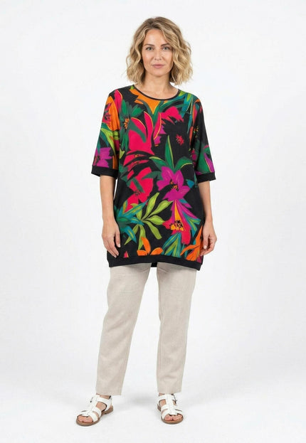 Дама в цял ръст, облечена в шарена лятна туника големи размери с ярък тропически флорален принт и къси ръкави.