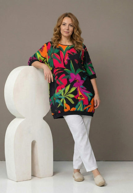 Шарена лятна туника големи размери с тропически флорален принт, представена в цял ръст от модел в комбинация с бели панталони.