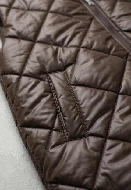 Детайлен кадър на шоколадово кафяв дълъг ватиран елек, показващ отблизо капитонираната на ромбове материя и страничния джоб.