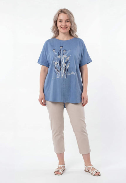 Синя лятна туника големи размери с детайлна флорална апликация отпред. Представена върху модел в цял ръст, съчетана със светъл панталон.