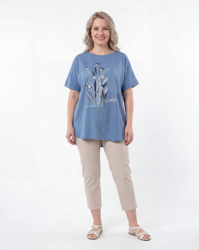 Синя лятна туника големи размери с детайлна флорална апликация отпред. Представена върху модел в цял ръст, съчетана със светъл панталон.