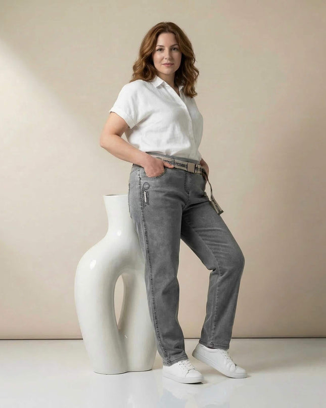 Дамски сиви макси дънки с права кройка и текстилен колан. Представени в цял ръст от модел с бяла риза, облегнат на декоративна фигура.