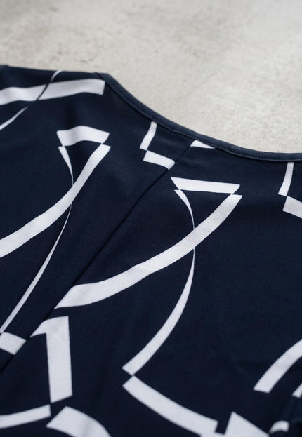 Детайл отблизо на гърба на тъмносиня официална макси рокля, акцентиращ върху шева и ефектния бял геометричен принт на меката материя.