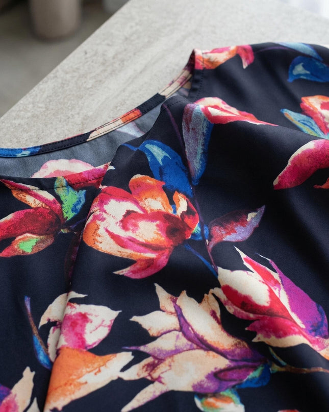 Детайл отблизо на тъмносиня официална макси туника, показващ ефирната материя с ярък флорален принт и обло деколте.