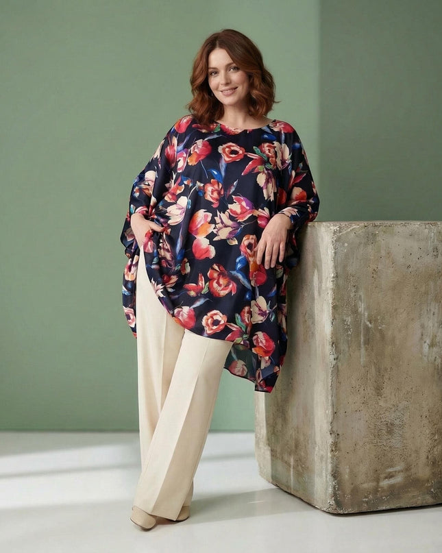 Жена в цял ръст, облечена в тъмносиня официална макси туника тип пончо с ярък флорален принт и асиметричен подгъв, съчетана със светъл панталон.